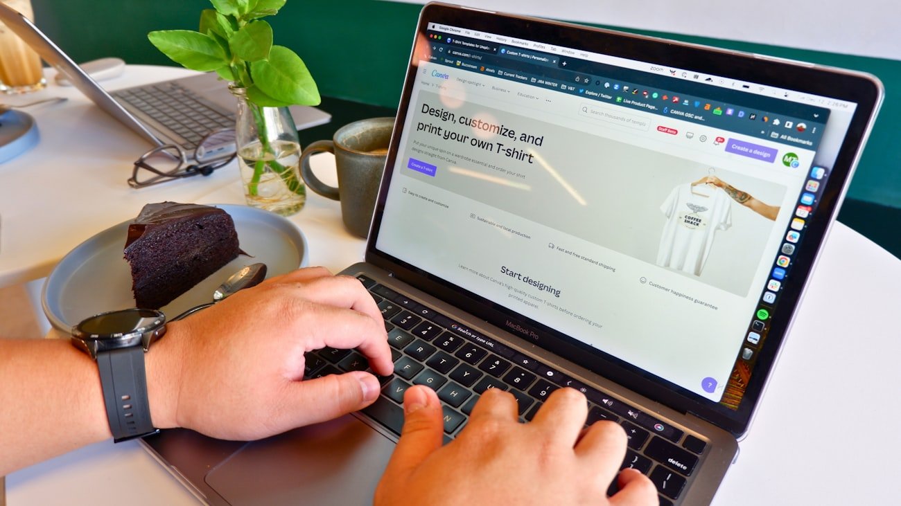 A person is using a laptop displaying a website for designing custom t-shirts. The hands on the keyboard suggest active work.